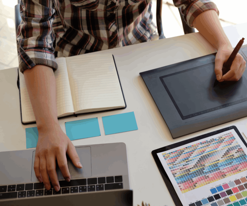 Man sitting at a desk doing graphic design with a laptop and color code pallet.